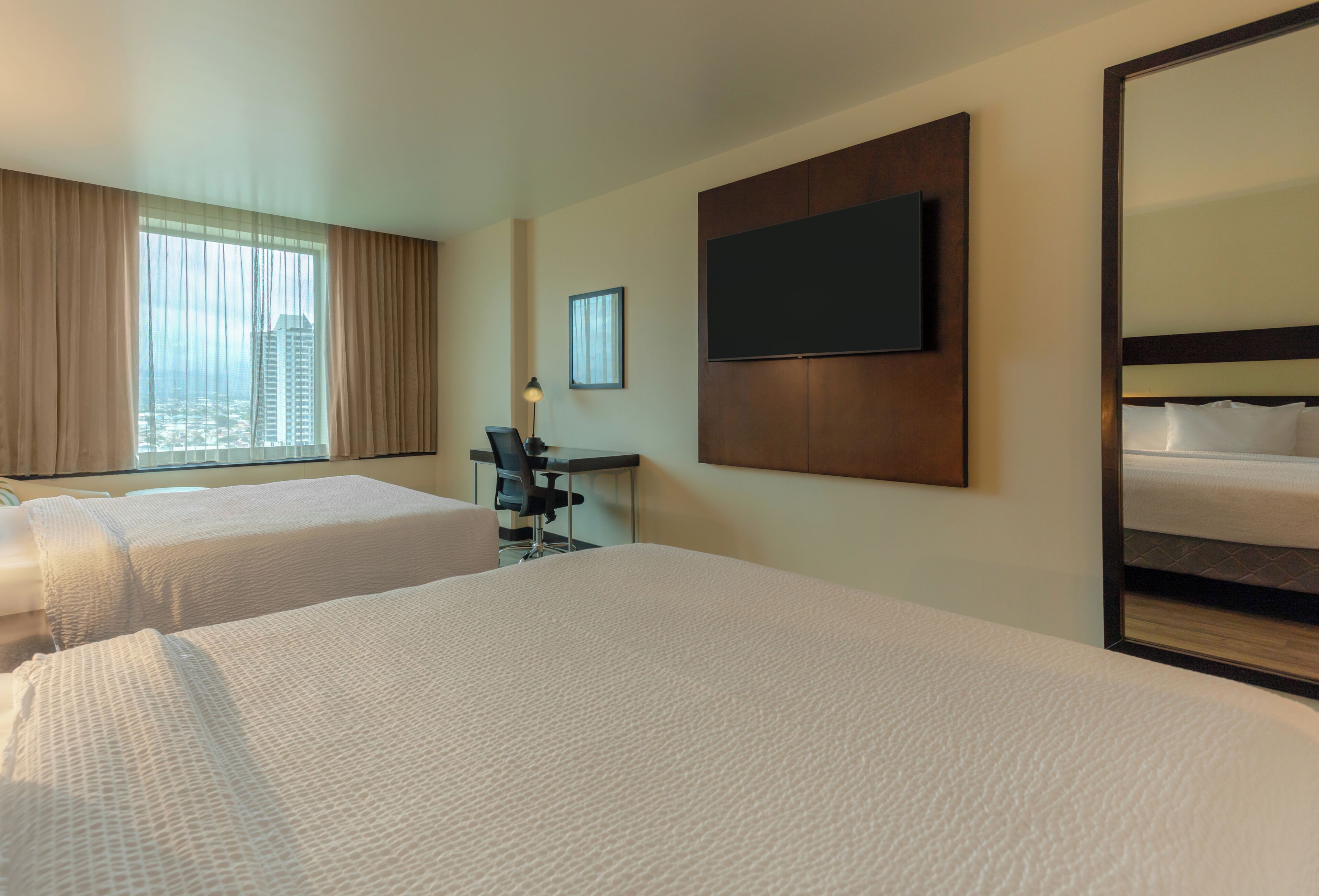 Une chambre d’hôtel avec deux lits, un bureau, une chaise, une télévision et un grand miroir.