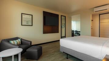 A hotel room with a bed, a sofa, a small table, a mirror, and an air conditioning unit.