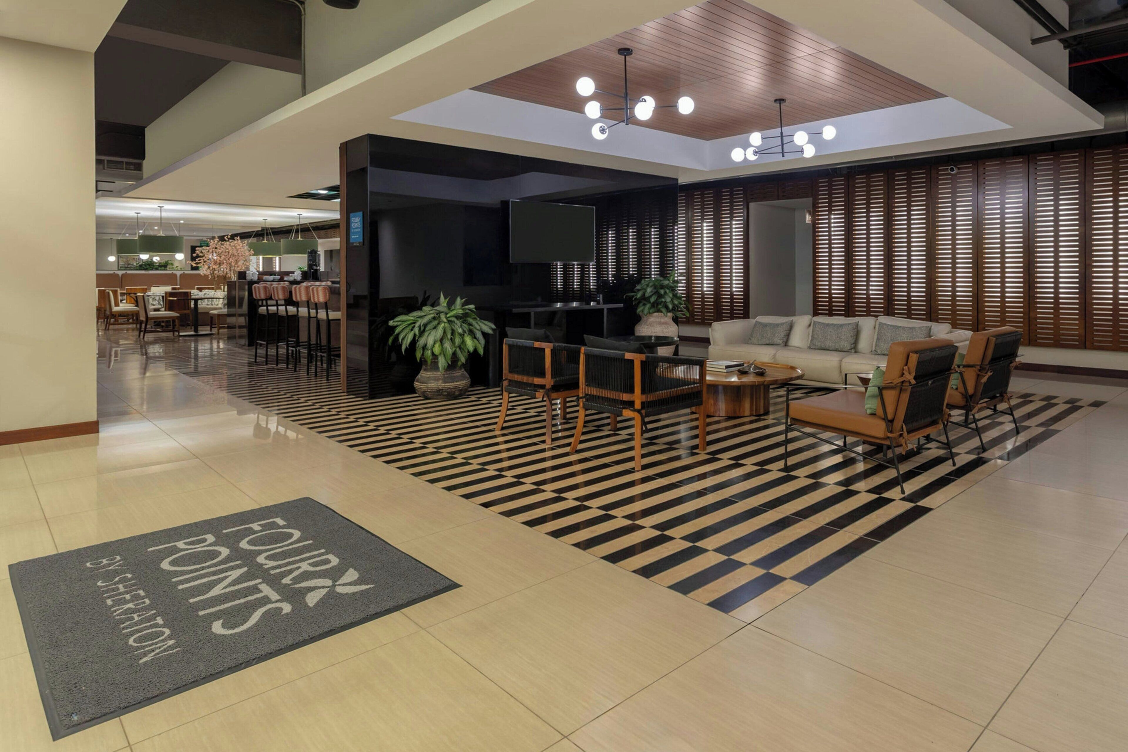 Un moderno vestíbulo de hotel con piso a cuadros, una recepción, un área de descanso y una pantalla de televisión.
