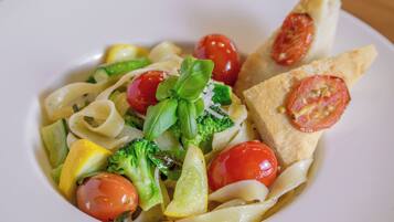 A plate of pasta with vegetables and a slice of bread.