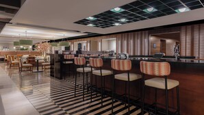 A modern bar area with high stools, a checkered floor, and a bar counter. - Four Points by Sheraton San Jose Sabana (San José)