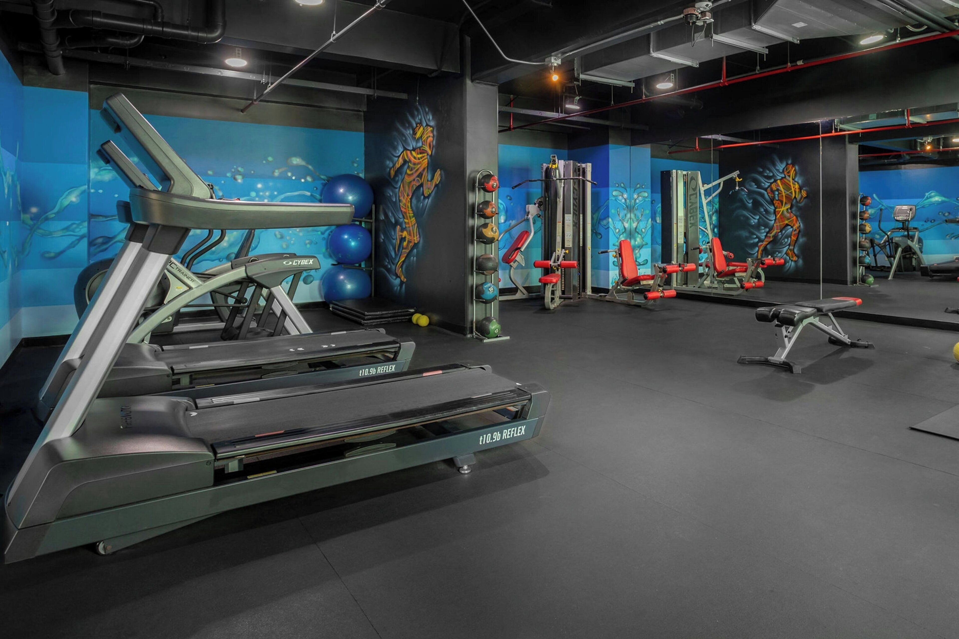 Une salle de sport équipée de tapis de course, d’appareils de musculation et de ballons d’exercice.