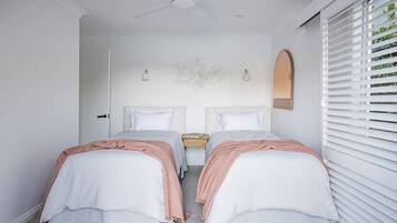 A bedroom with two beds, a ceiling fan, a nightstand, and a window with blinds.