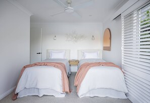 A bedroom with two beds, a ceiling fan, a nightstand, and a window with blinds. - Calabash Bay Lodge (Berowra Waters)