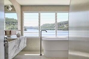 A modern bathroom with a large bathtub, a marble vanity, and a view of a lake. - Calabash Bay Lodge (Berowra Waters)