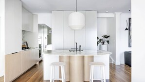 Una cucina moderna con isola centrale, due sgabelli bianchi e un lampadario a sospensione.