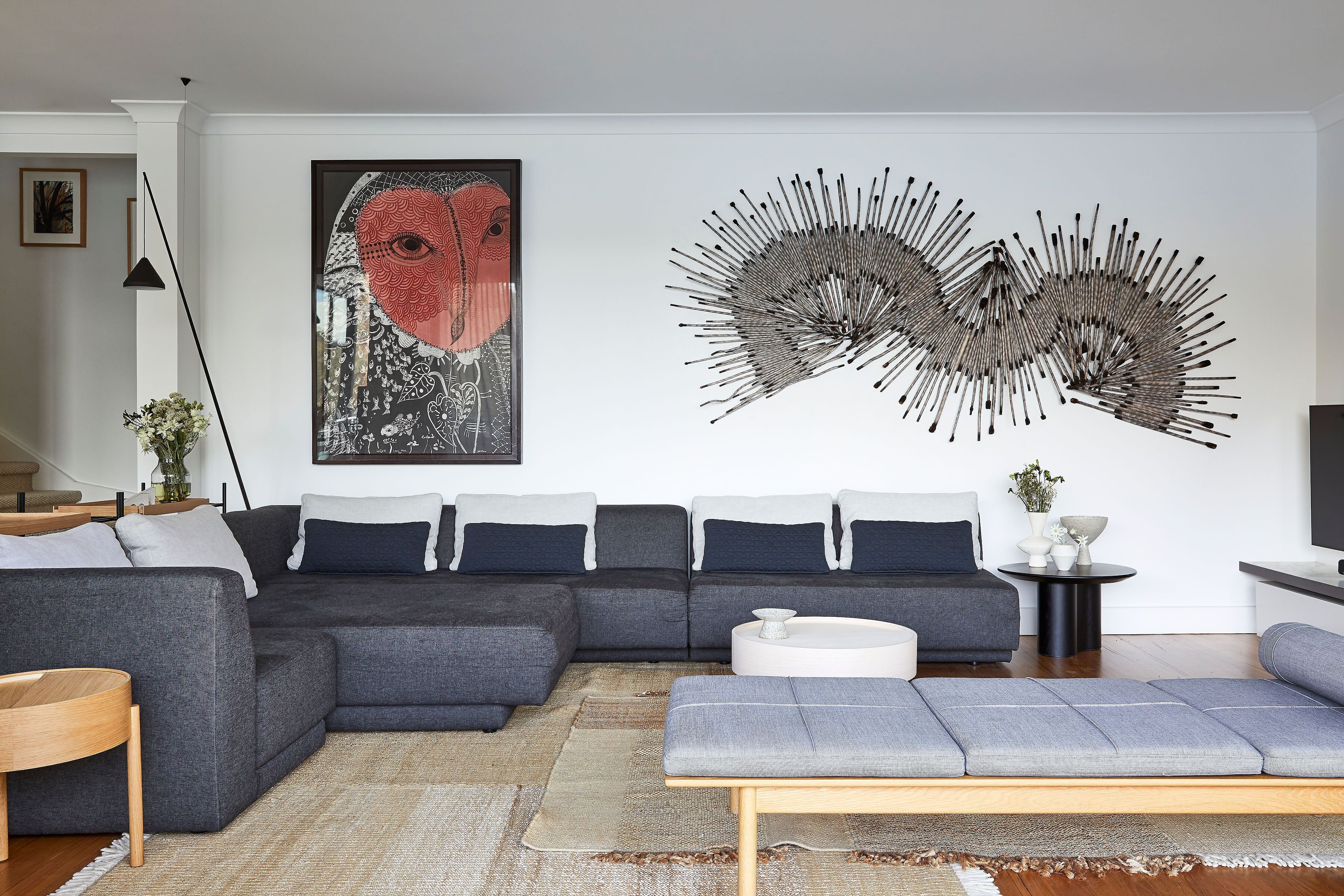 A modern living room with a sectional sofa, a round coffee table, and a large abstract wall art piece.
