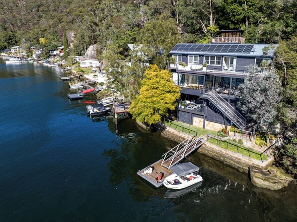 A lakeside property with a dock, a boat, and a house with solar panels. - Calabash Bay Lodge (Berowra Waters)
