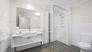 A modern bathroom with a glass-enclosed shower, a white sink with a mirror above it, and a toilet.