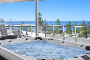 Una bañera de hidromasaje en un balcón con vista al océano y a árboles.