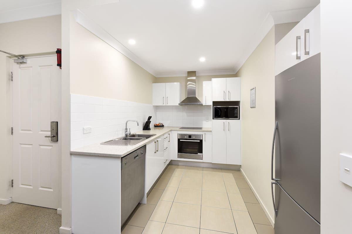 A modern kitchen with white cabinets, stainless steel appliances, and a tiled floor.