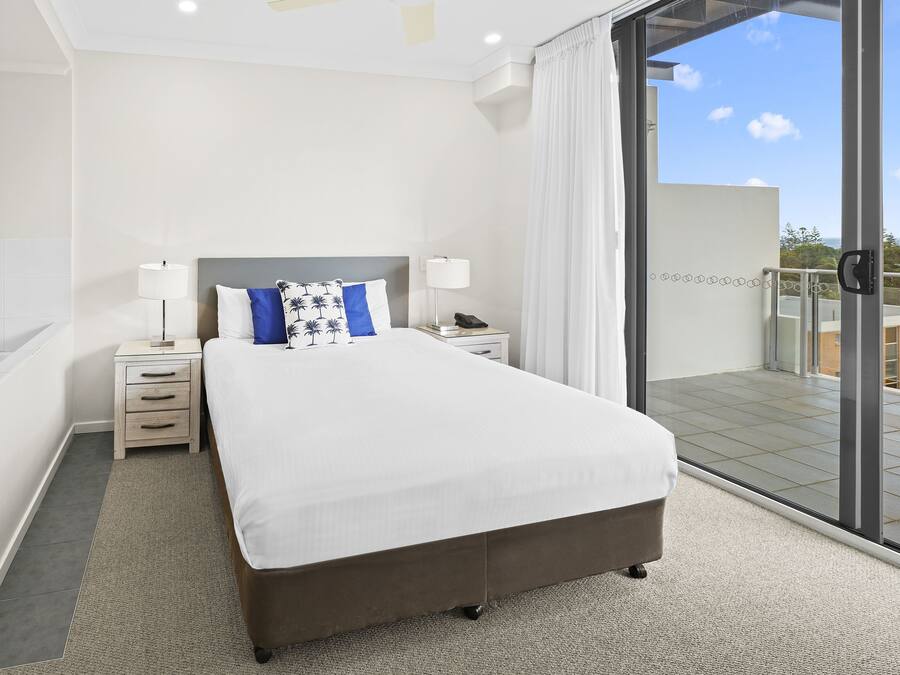 Una camera d'hotel moderna con un letto grande, comodini, un tavolino da notte e vista sulla città grazie a finestre a tutta parete.
