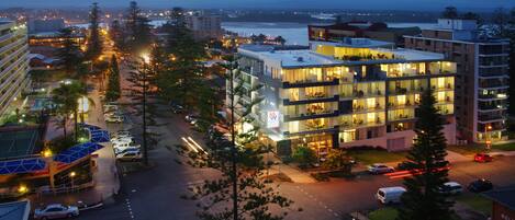 A modern hotel with multiple floors, large windows, and a parking area with cars.