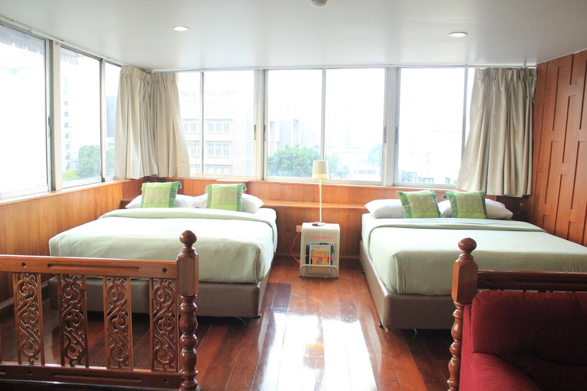 A hotel room with two beds, wooden headboards, a small table, and a red chair.