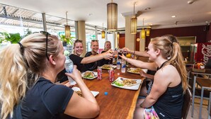 Un grupo de personas sentadas alrededor de una mesa de madera en un restaurante, con luces colgantes y un refrigerador de Coca-Cola al fondo.