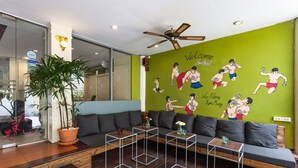 Un área de estar moderna con un mural de pared verde, un ventilador de techo y un sofá con una mesita de centro.