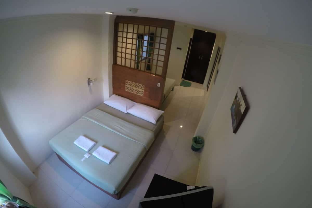 A small, single-bed room with a wooden headboard, a bedside table, and a green trash bin.