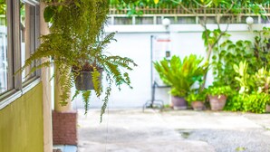 Un espacio al aire libre techado con plantas colgantes, un banco de madera y suelo de concreto.
