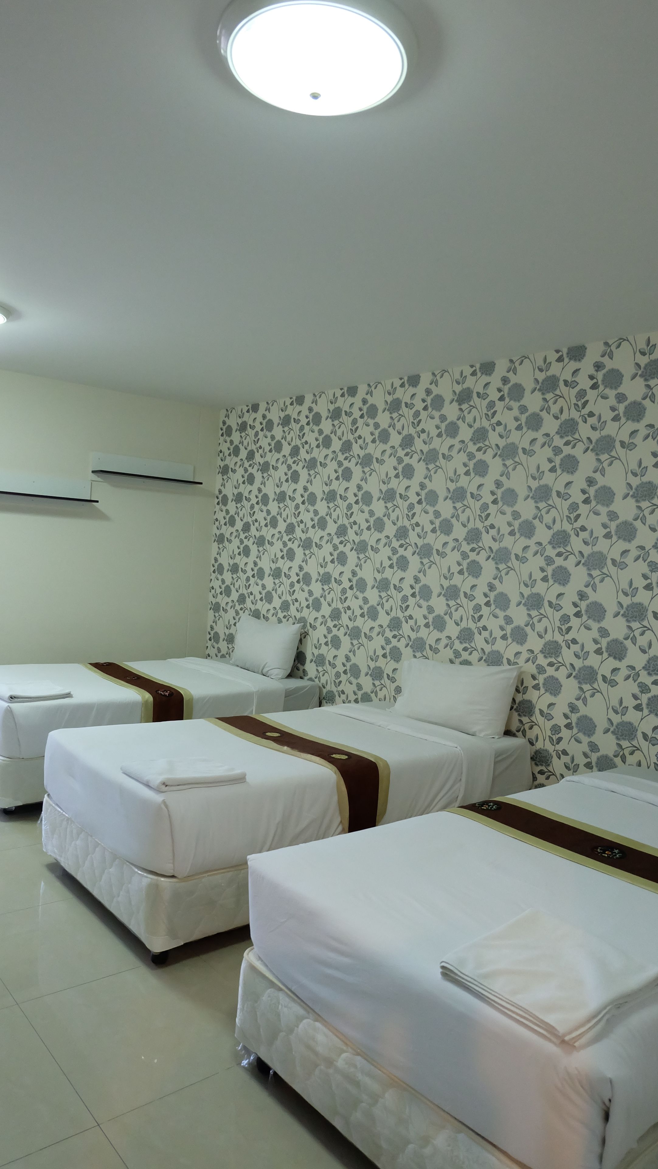 Une chambre d’hôtel avec trois lits simples, un papier peint à motifs floraux et un luminaire au plafond.