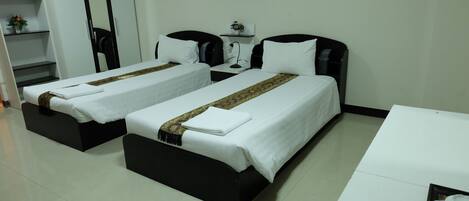 A hotel room with two single beds, a small table, a nightstand, and a shelf with flowers.