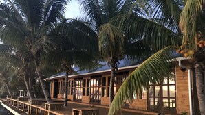A wooden deck with benches overlooking a body of water, surrounded by palm trees and a wooden building with large windows. - Jet Over Hotel (Salelologa)