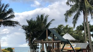 A playground with a slide and climbing area, surrounded by palm trees and a beach view. - Jet Over Hotel (Salelologa)