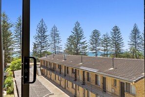 Un motel avec une longue rangée de chambres, un espace extérieur abrité et une vue sur de grands arbres et une étendue d’eau.