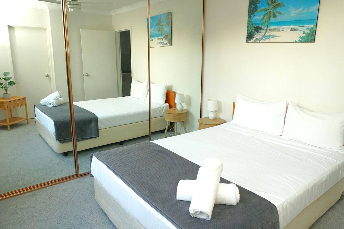 Quarto de hotel com duas camas, um espelho grande e obra de arte retratando uma cena de praia.