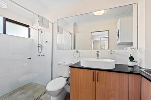 Une salle de bain moderne avec une douche à parois de verre, des toilettes blanches, un lavabo avec un miroir au-dessus et des meubles en bois.