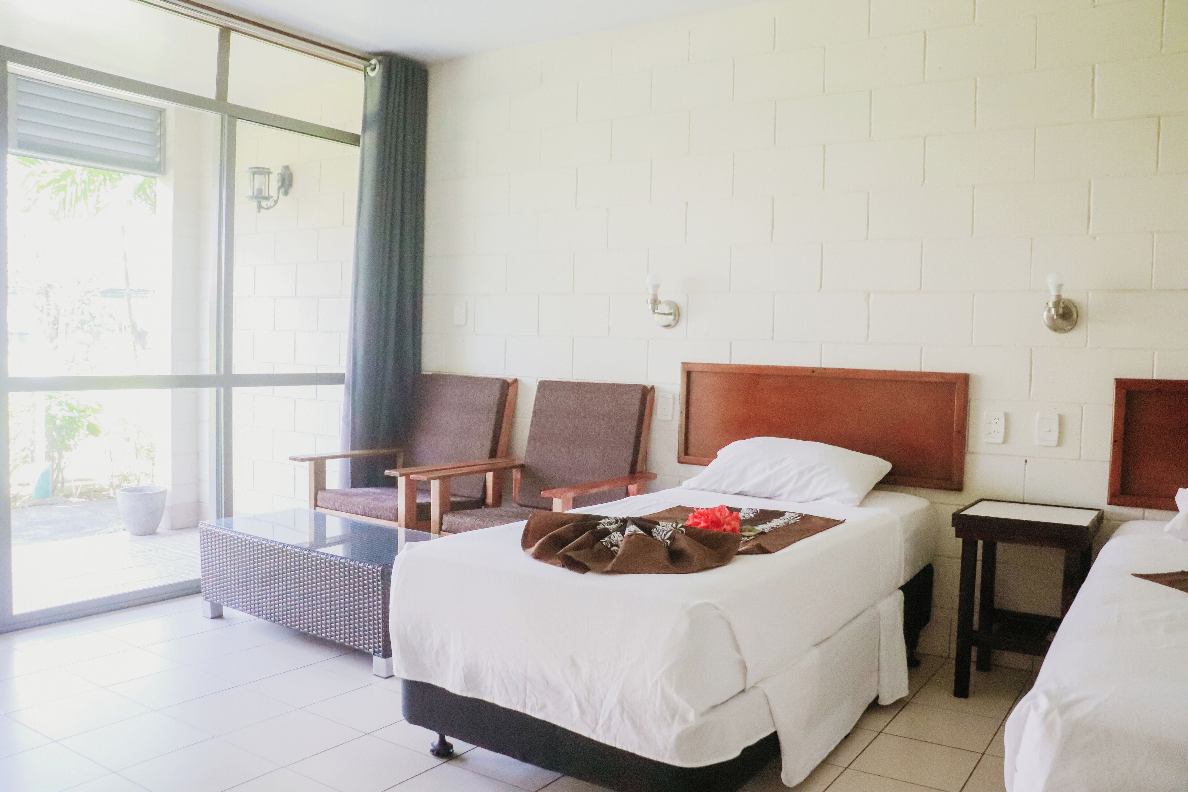A hotel room with a large bed, two armchairs, a small table, and a view through a glass door.