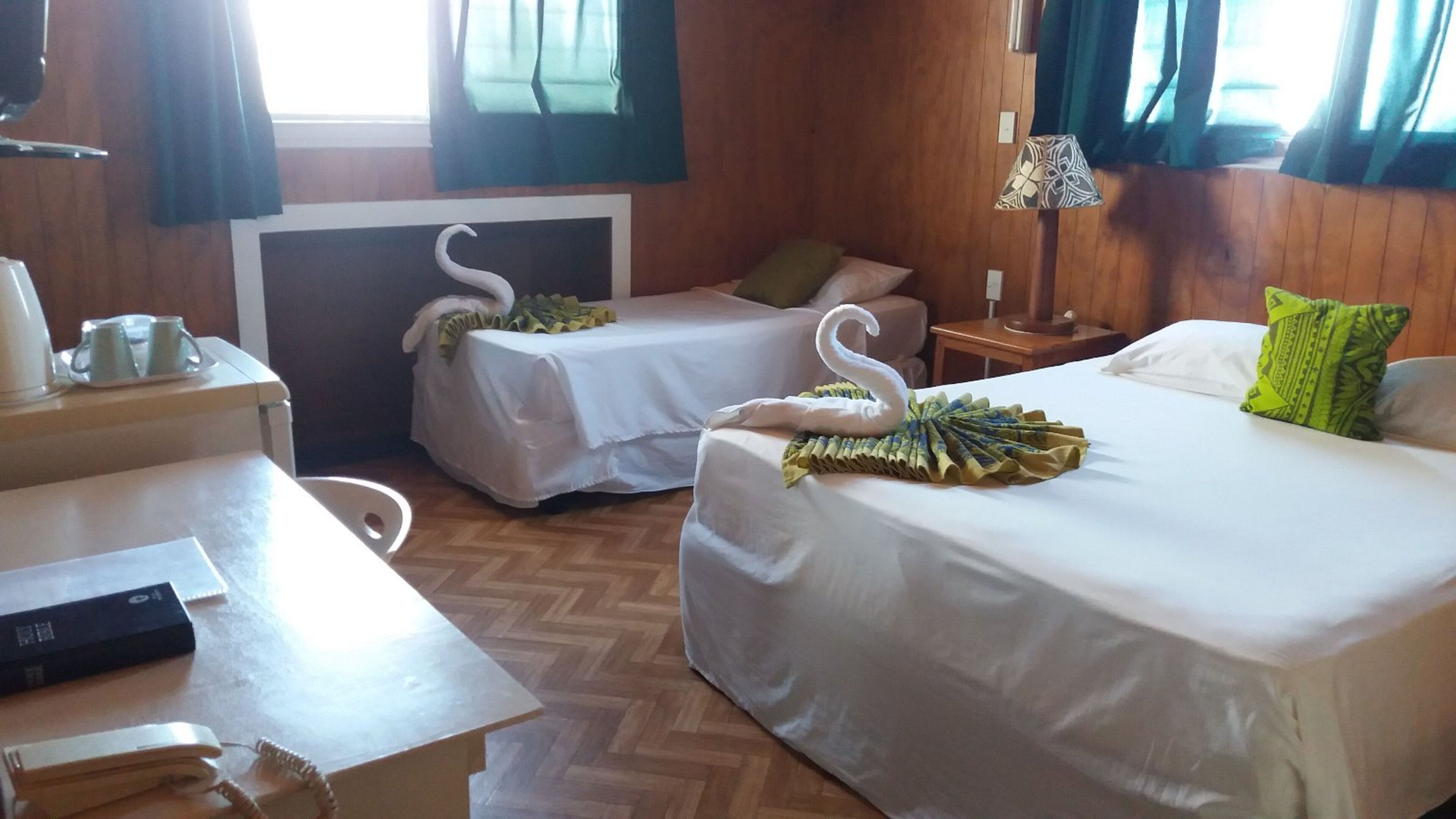 A hotel room with two beds, a desk, a chair, a lamp, and a window with curtains.