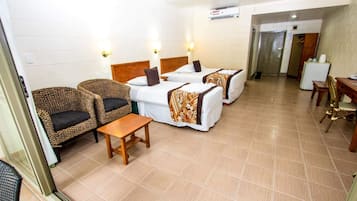 A hotel room with two beds, wicker chairs, a wooden table, and a small desk.