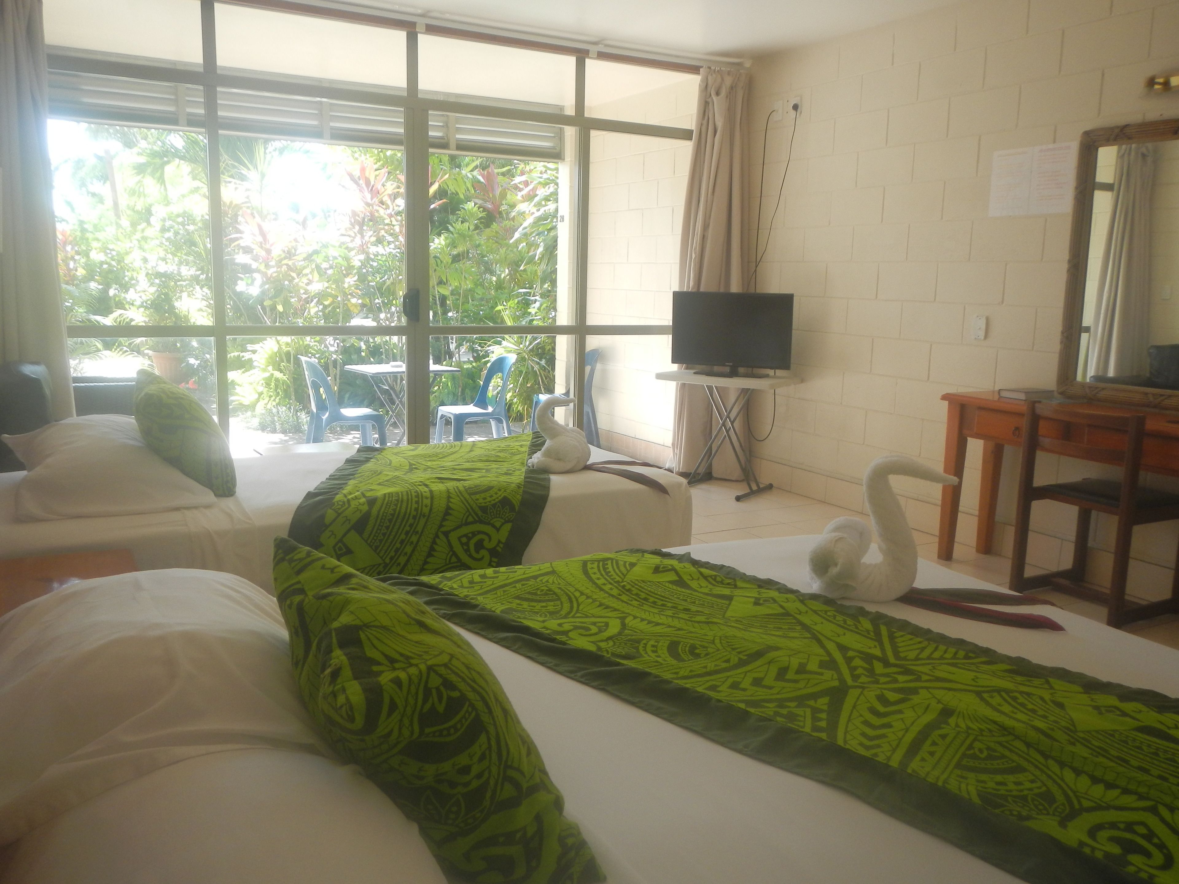 Quarto de hotel com duas camas, televisão, escrivaninha e vista para o verde lá fora.