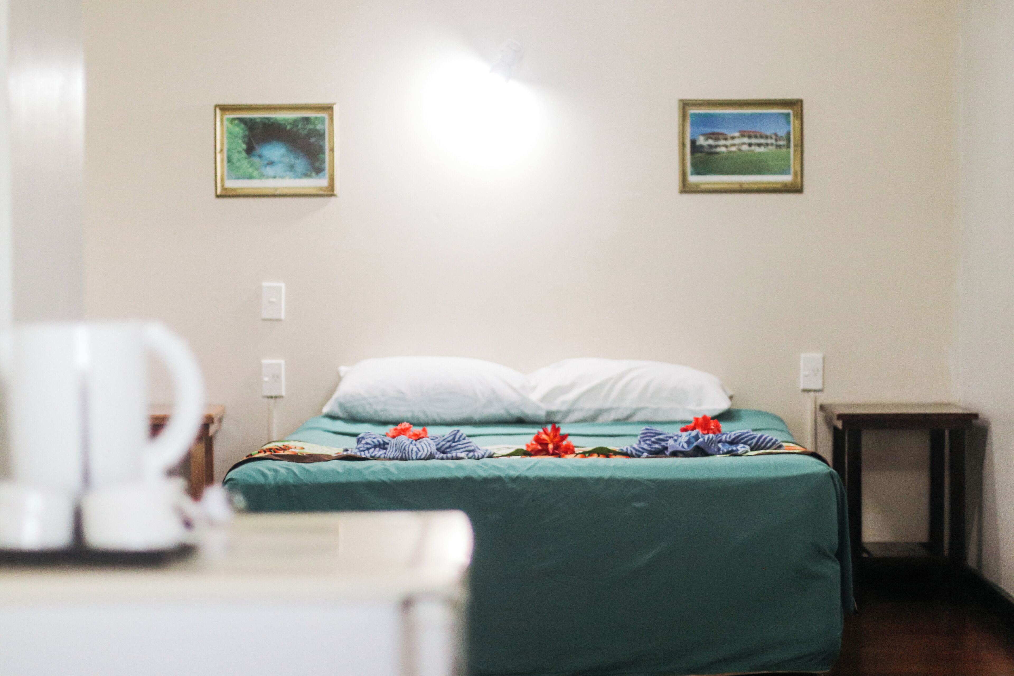 A hotel room with a bed, a bedside table, and two framed pictures on the wall.