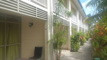 A corridor with a chair, potted plants, and a building with balconies and a tiled exterior.