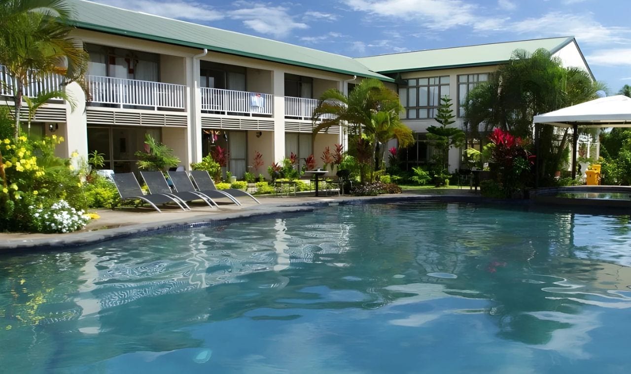 A hotel with a swimming pool, balconies, and tropical landscaping.