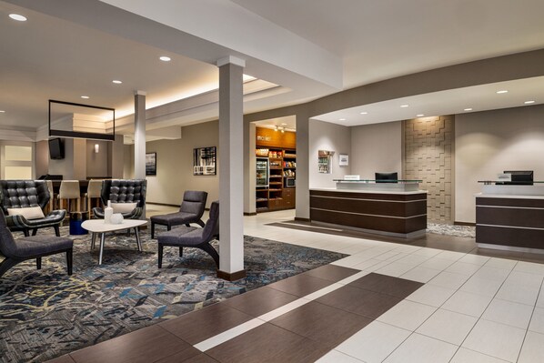 A hotel lobby with leather chairs, a reception desk, and a coffee station.