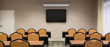 A conference room with a large screen, multiple tables, and chairs.