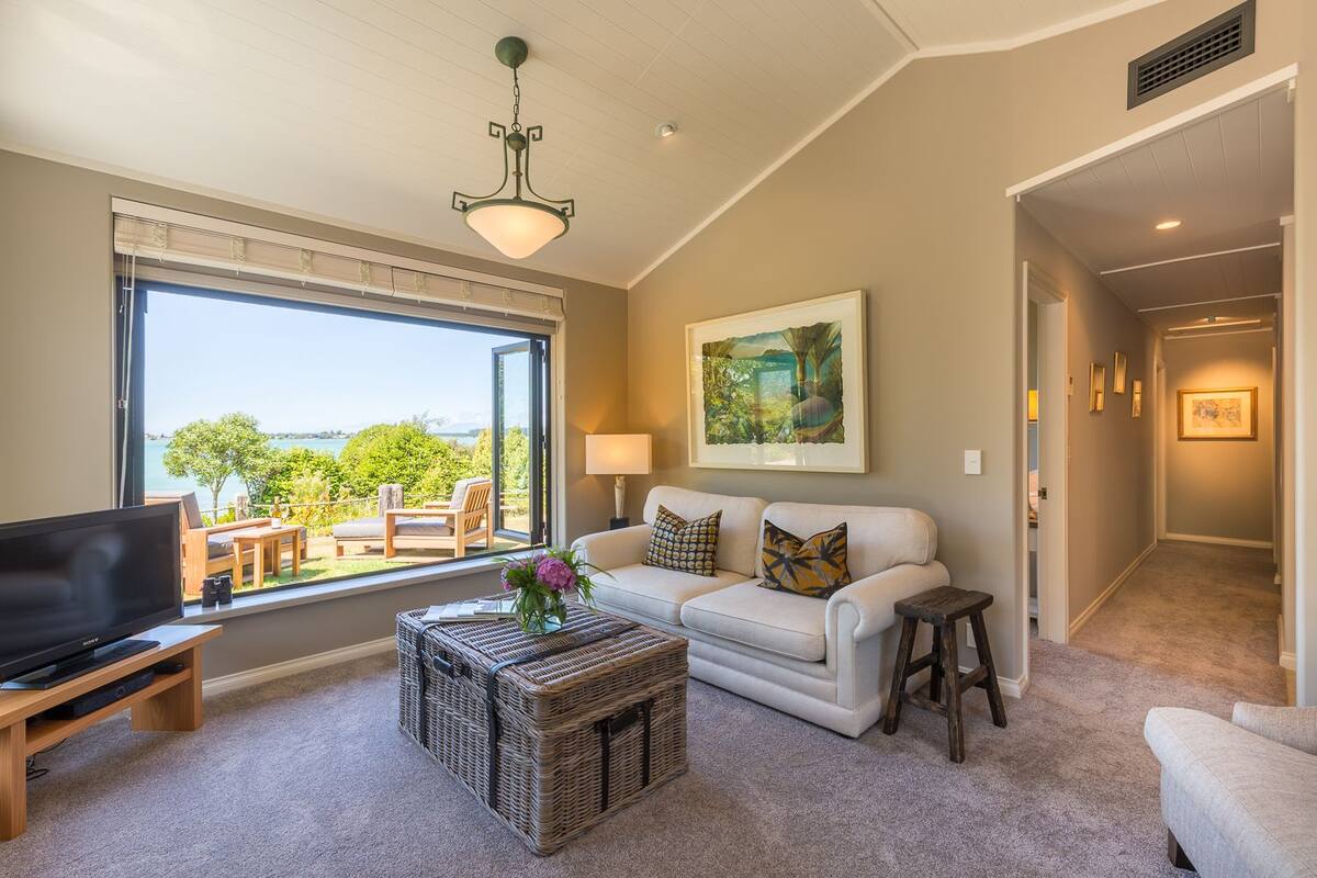A living room with a sofa, a television, a wicker coffee table, and a view of the outdoors.