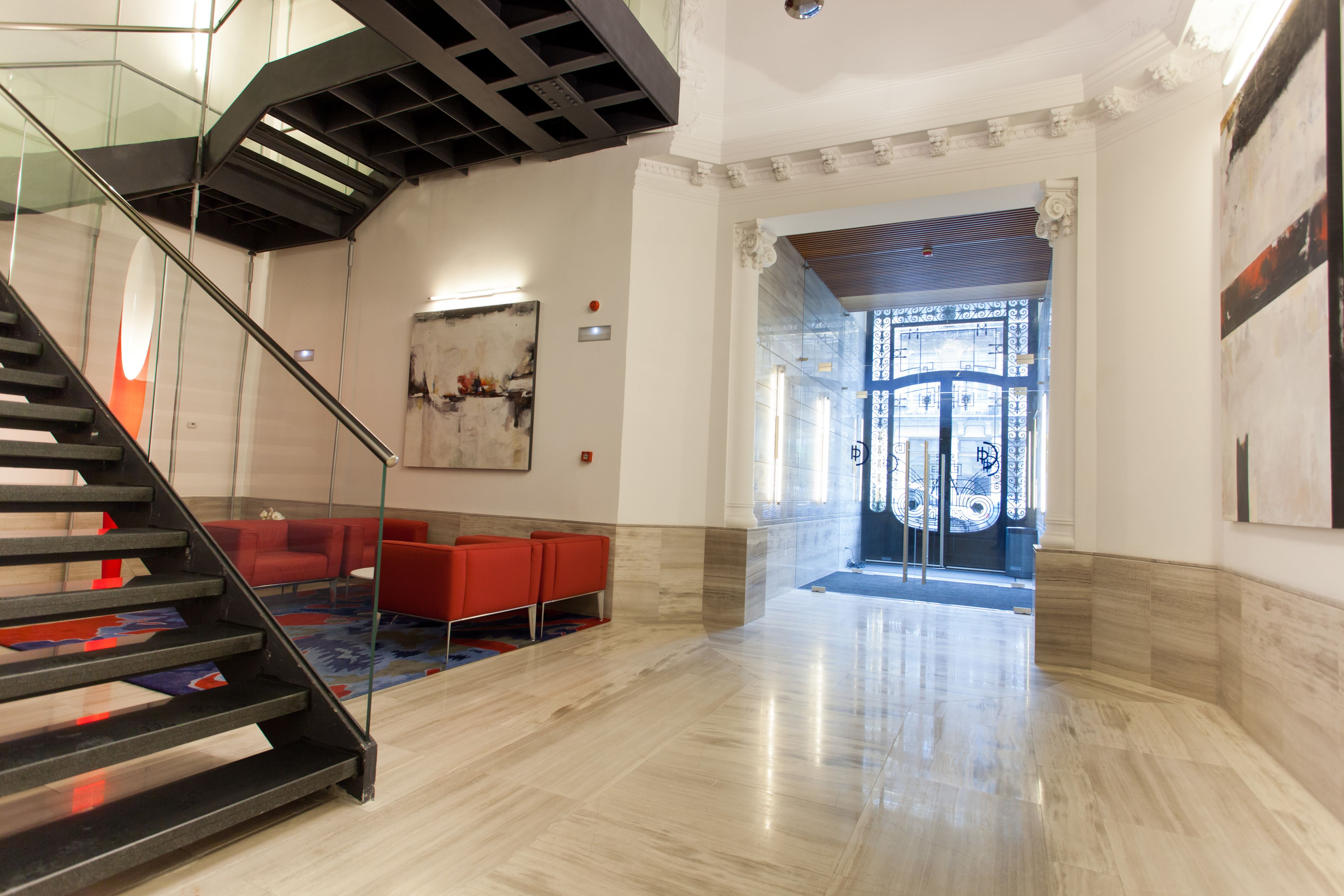 A modern lobby with a glass staircase, red seating, and a decorative door.