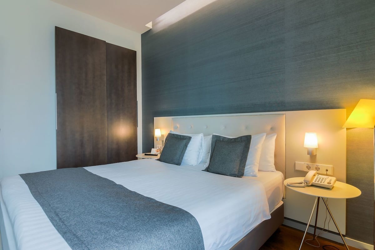 A hotel room with a large bed, bedside lamps, a phone, and a wall-mounted light.