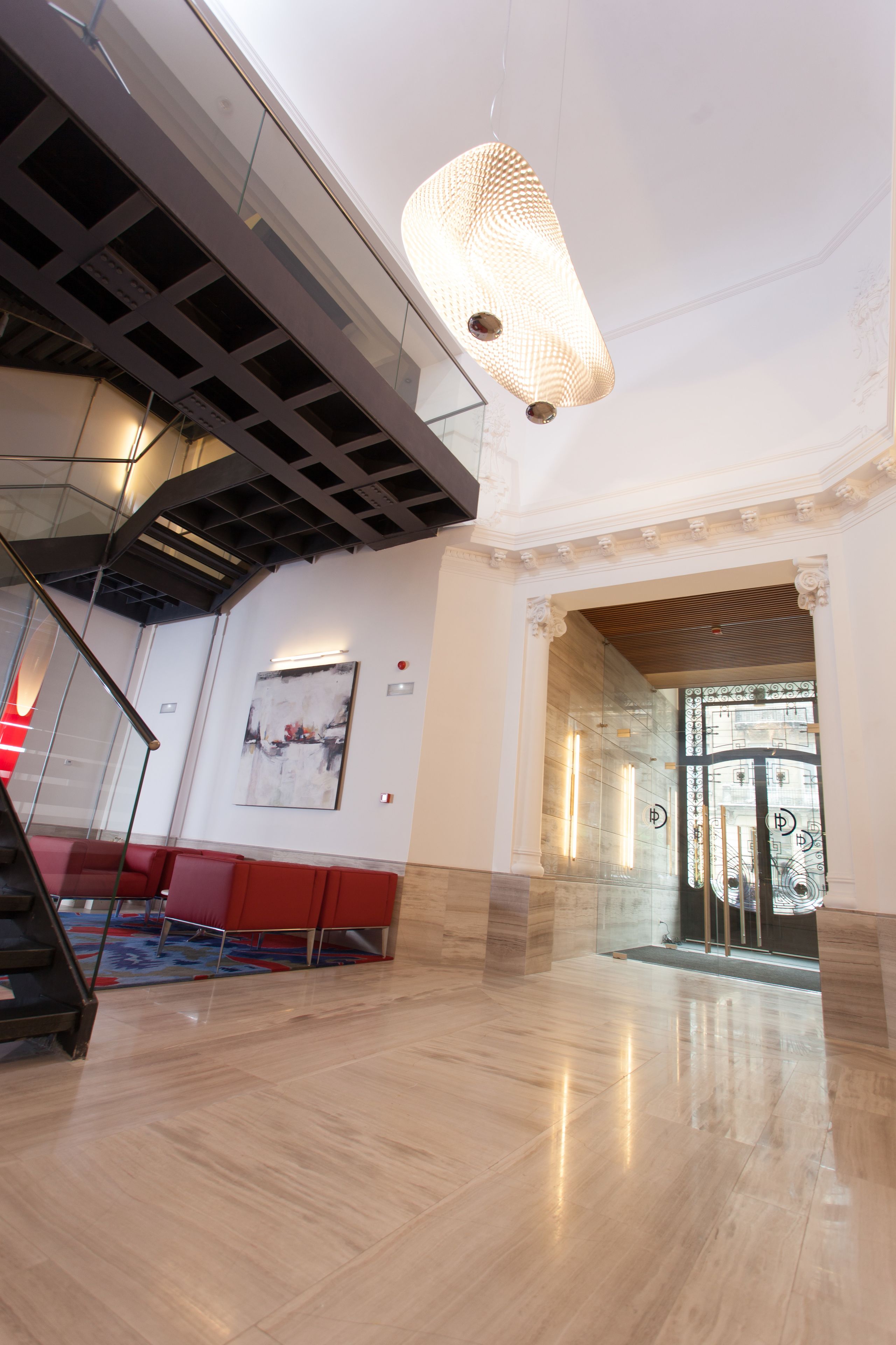 A spacious lobby with a modern staircase, a large abstract painting, and a glass door entrance.