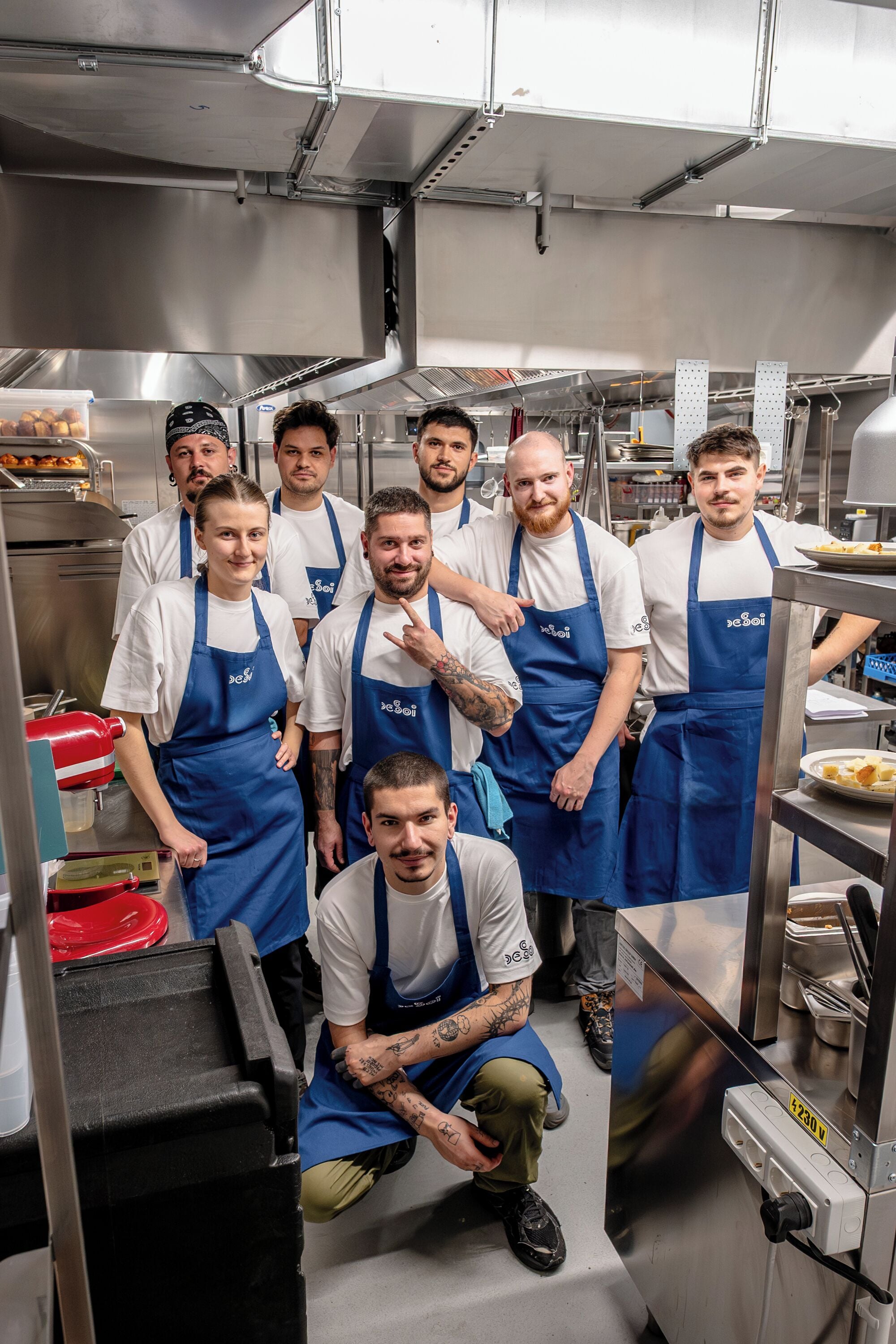 Un grupo de personas en una cocina con electrodomésticos de acero inoxidable y una exhibición de alimentos.
