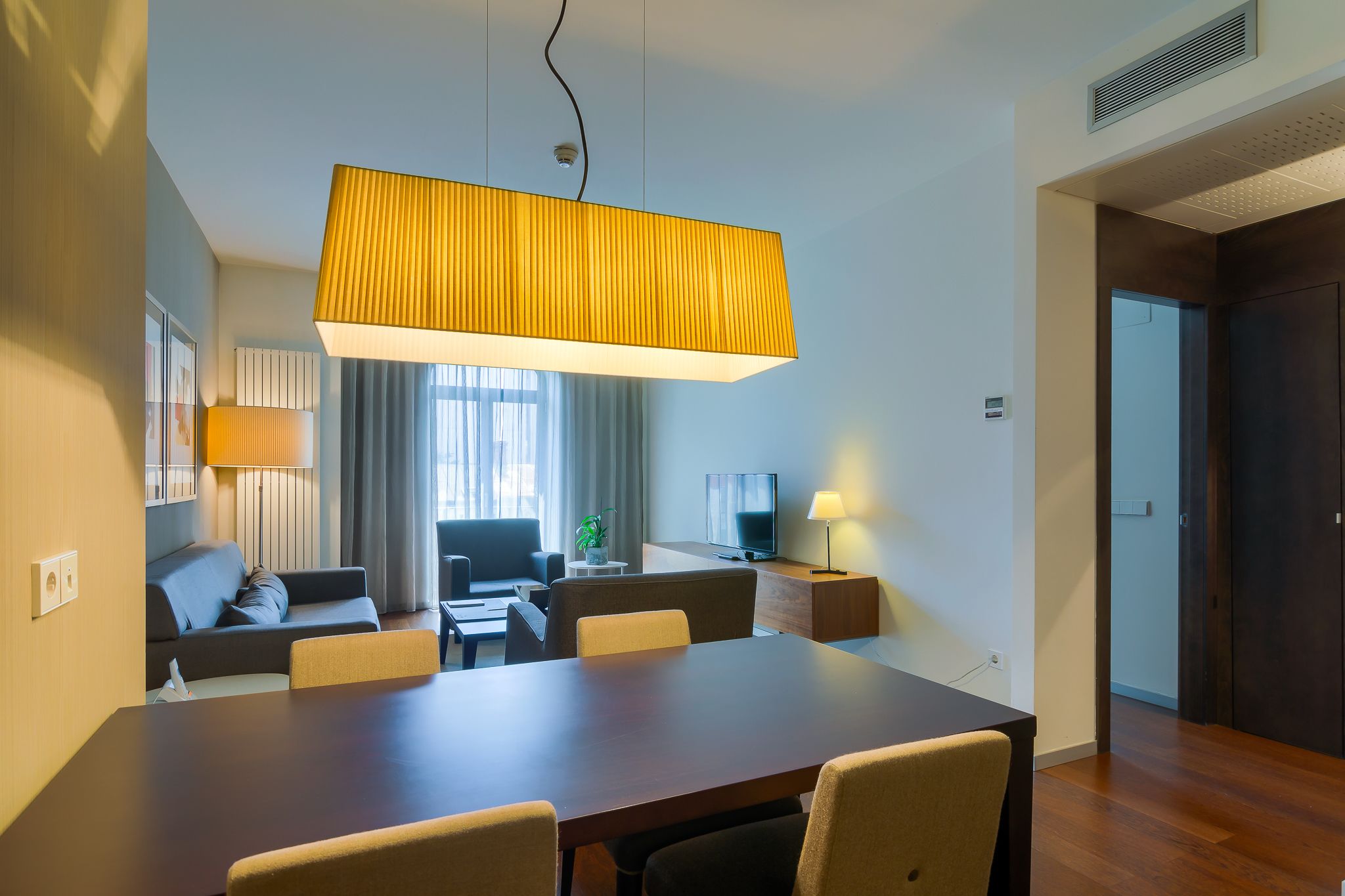 Ein modernes Hotelzimmer mit Essbereich, einer Couch, einem Fernseher und einem großen Fenster.
