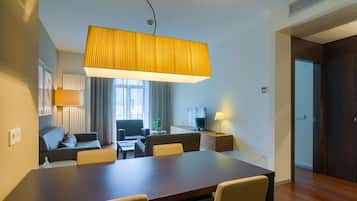 Ein modernes Hotelzimmer mit Essbereich, einer Couch, einem Fernseher und einem großen Fenster.
