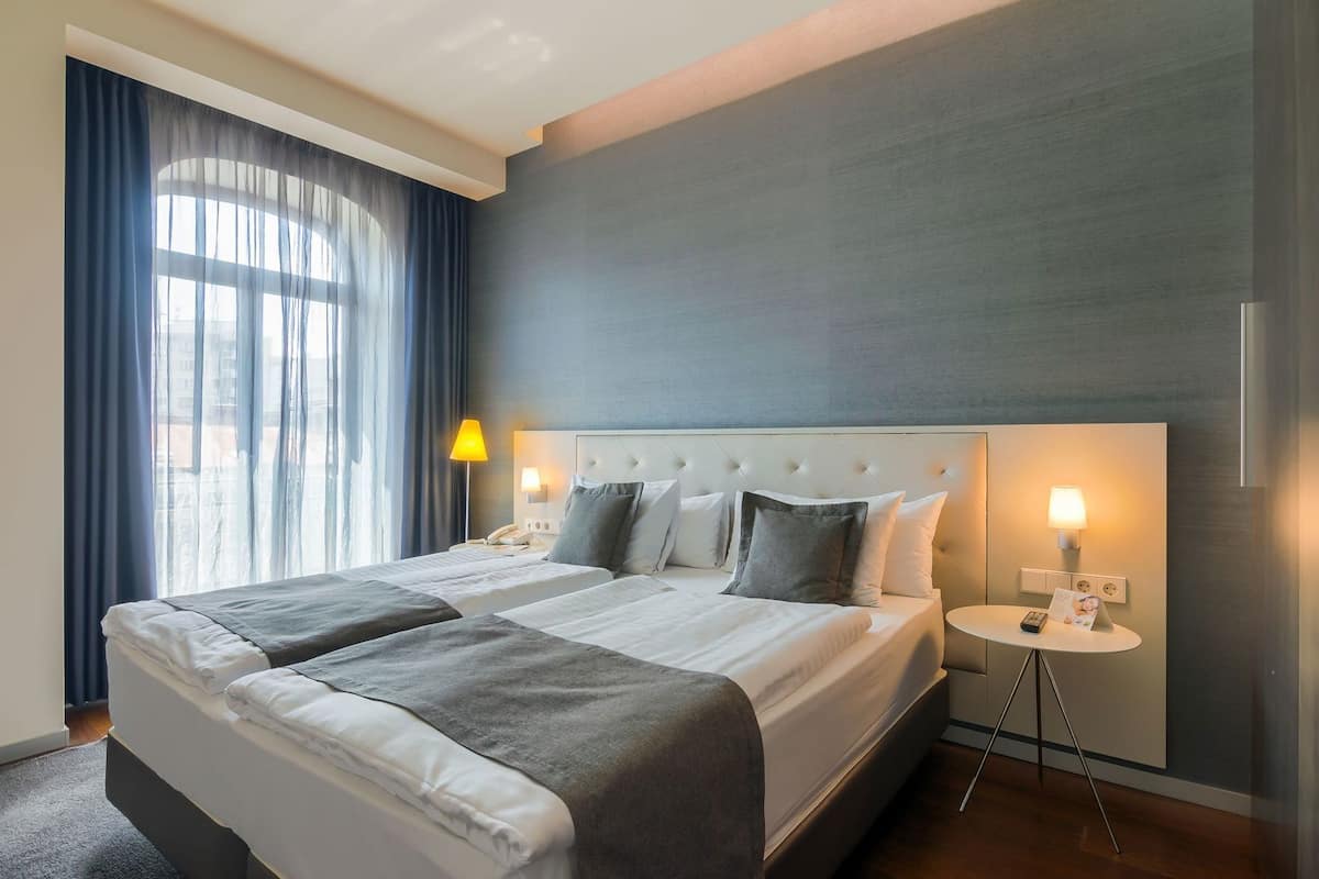 A hotel room with a large bed, two bedside tables, a nightstand, and a window with curtains.