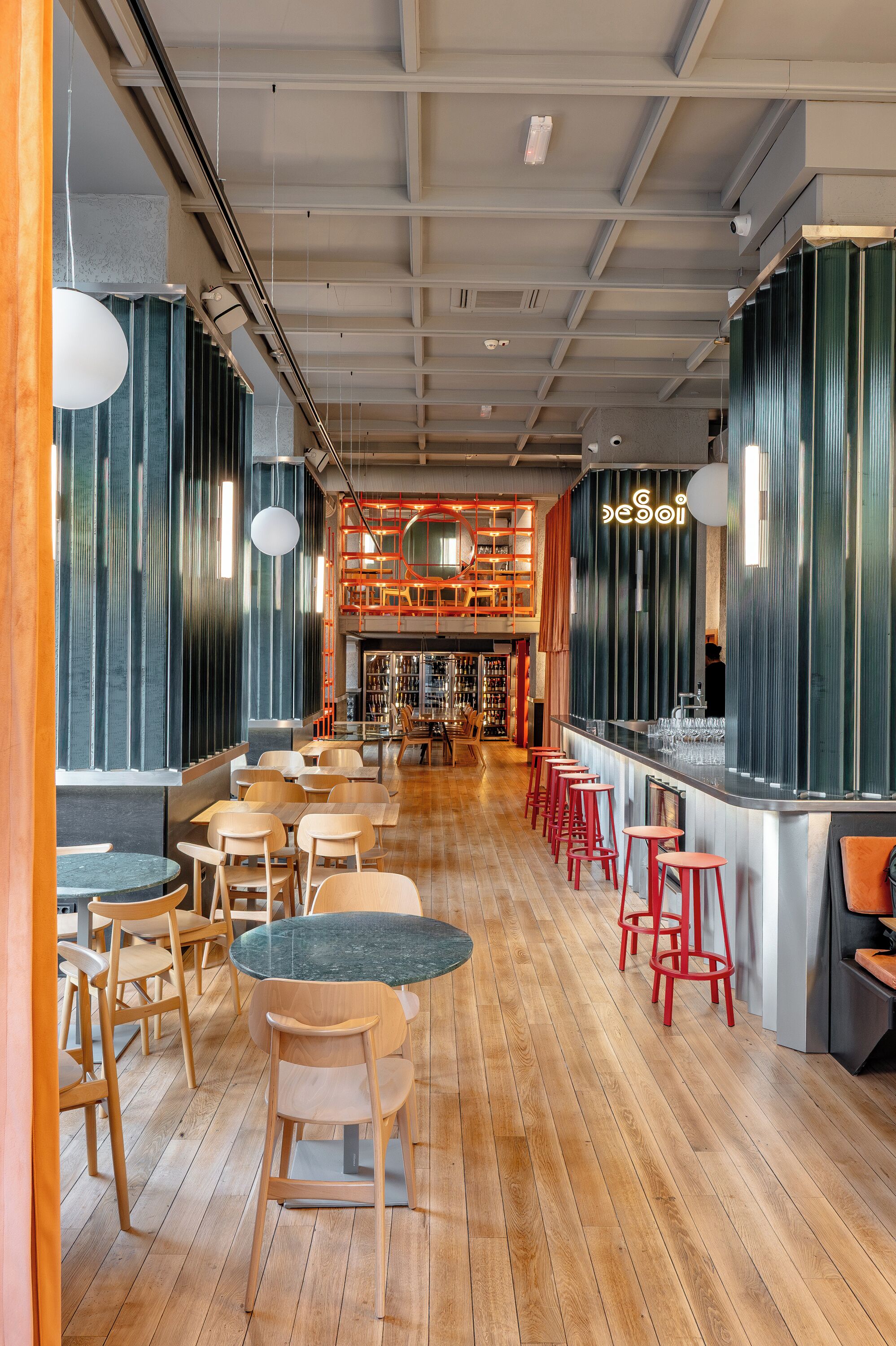 A modern bar area with wooden flooring, red bar stools, and a variety of seating options including tables and chairs.