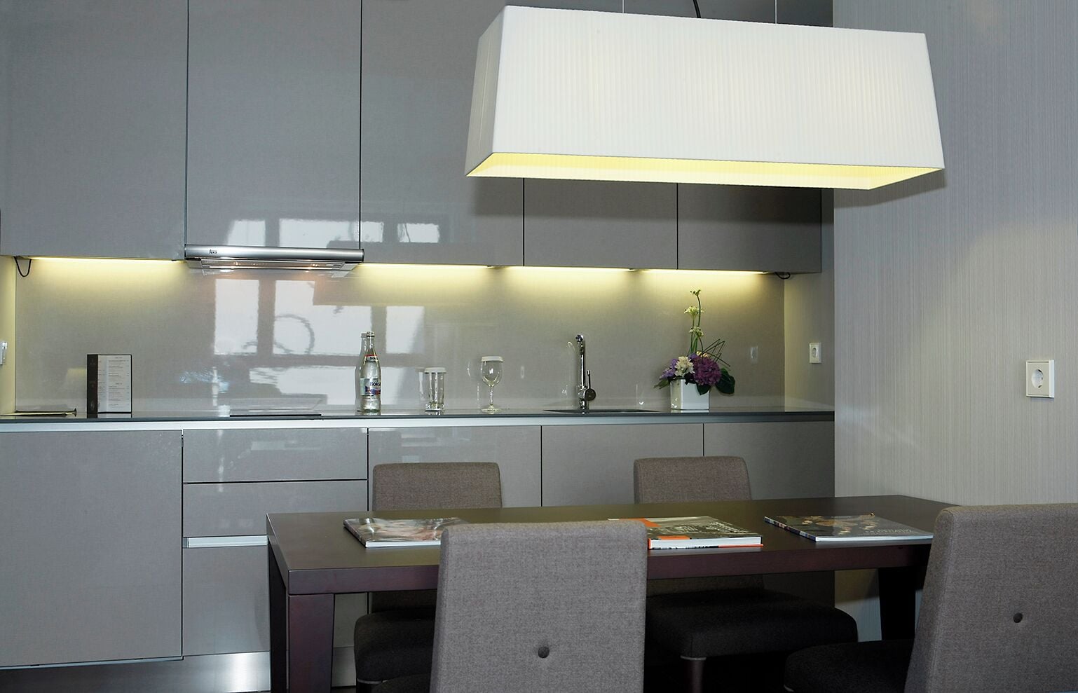 A modern kitchen with a dining area, featuring a large island, grey cabinetry, and a pendant light.