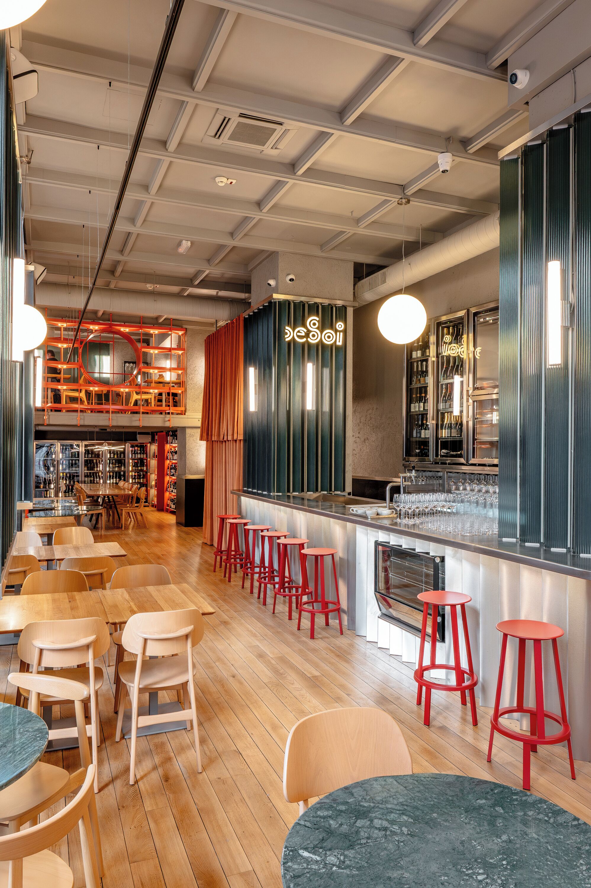 A modern bar with wooden floors, red bar stools, and a variety of seating options including tables and chairs.