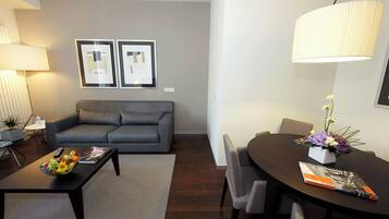 A modern living room with a grey sofa, a coffee table with fruit, a dining table with chairs, and a lamp.